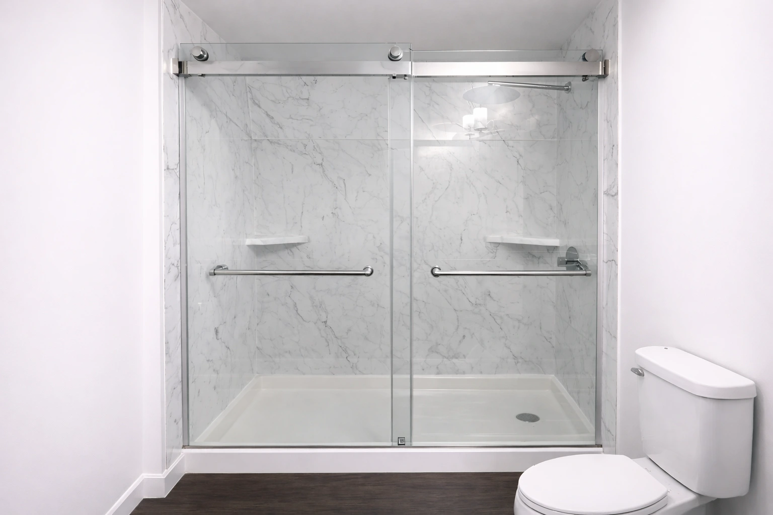 Frameless glass shower enclosure with sliding doors, white marble look wall panels, built in corner shelves, dual grab bars, and a white shower base next to a modern white toilet.