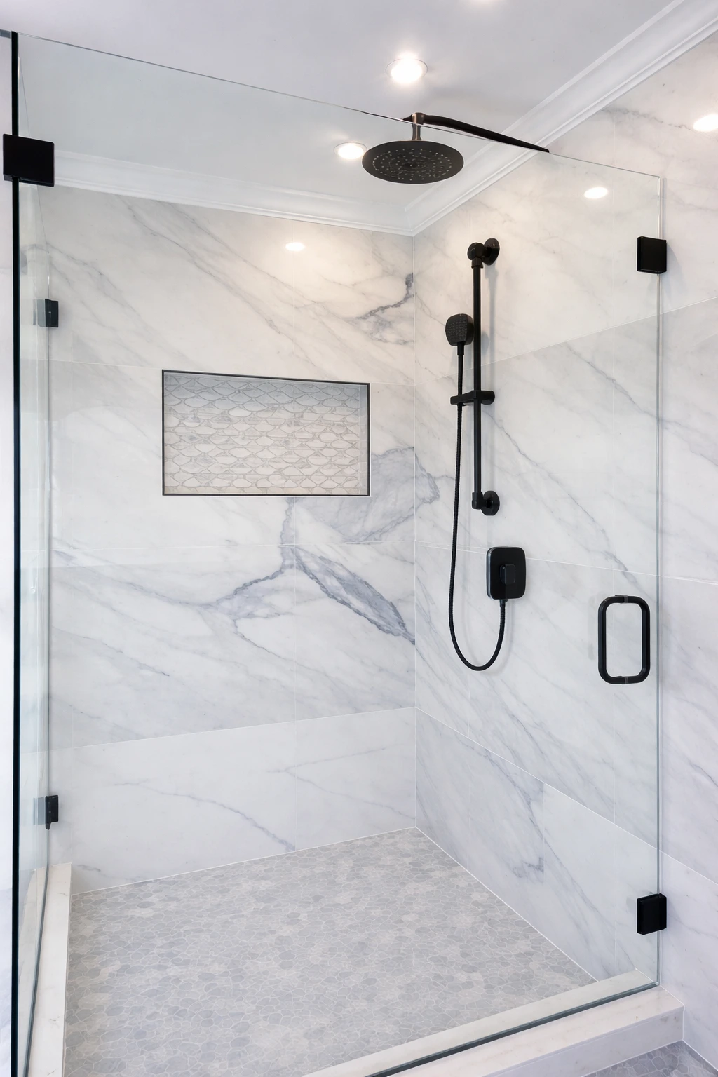 Frameless walk-in shower with marble wall tile and black fixtures in a modern bathroom remodeling project in Marlboro, NJ.