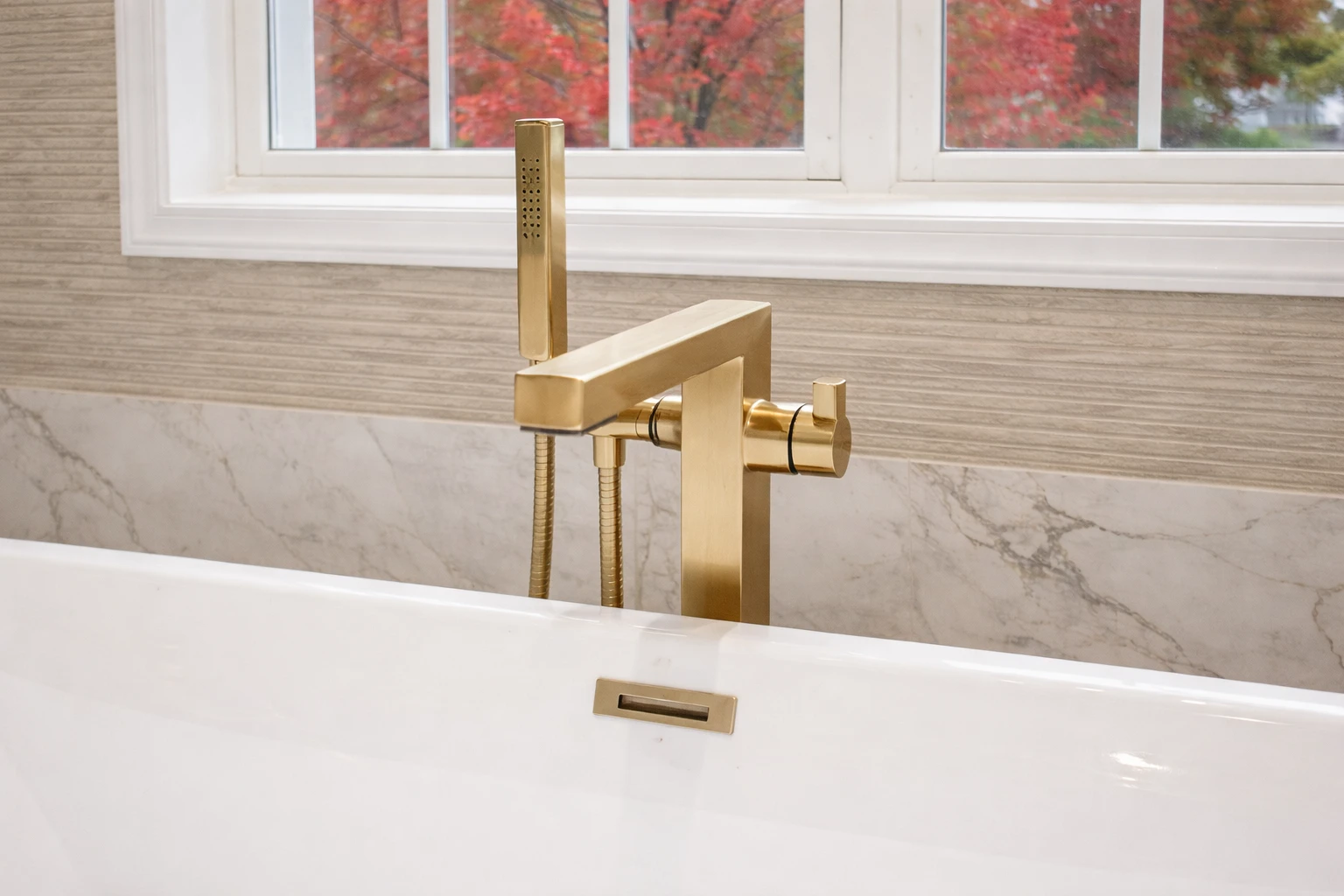 Brushed brass freestanding tub faucet installed beside a modern soaking tub as part of a luxury bathroom remodeling project in Morganville, NJ.
