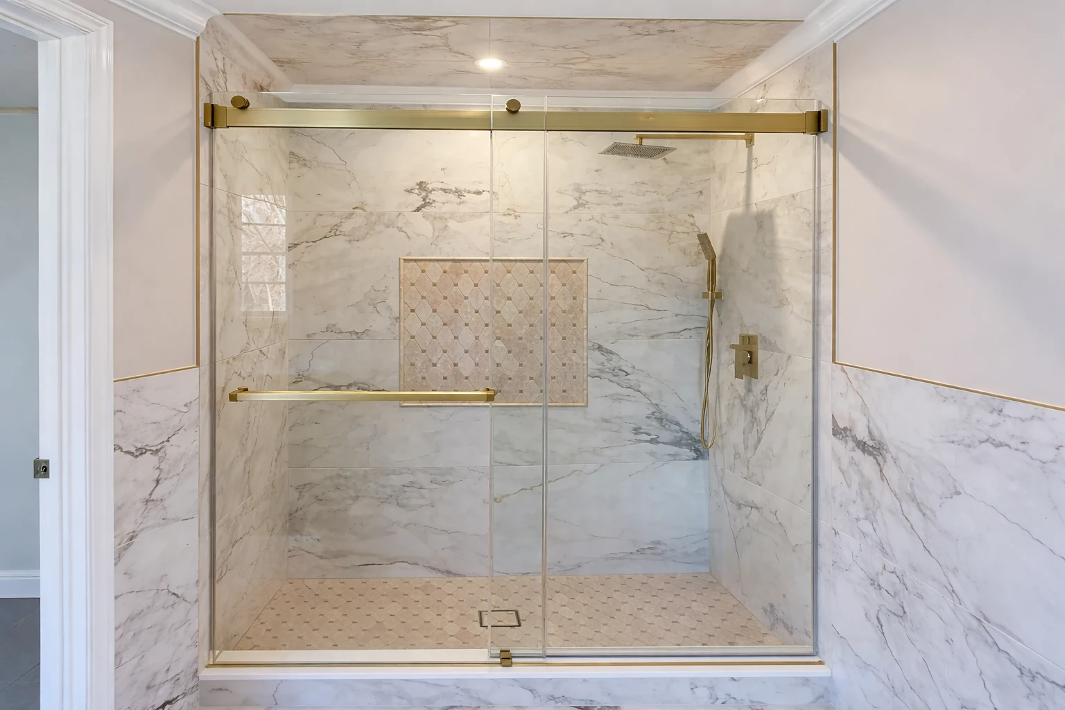 Spacious frameless glass shower with marble walls and brass hardware in a high-end bathroom remodeling project in Morganville, NJ.
