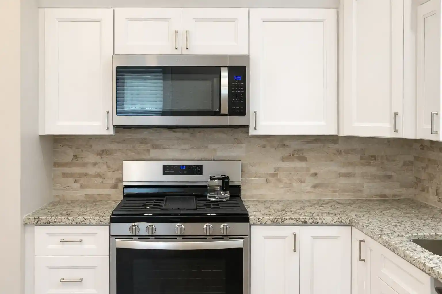 Modern kitchen remodeling in Neptune City, NJ showcasing a stainless steel gas range, built-in microwave, white cabinetry, and textured stone backsplash.
