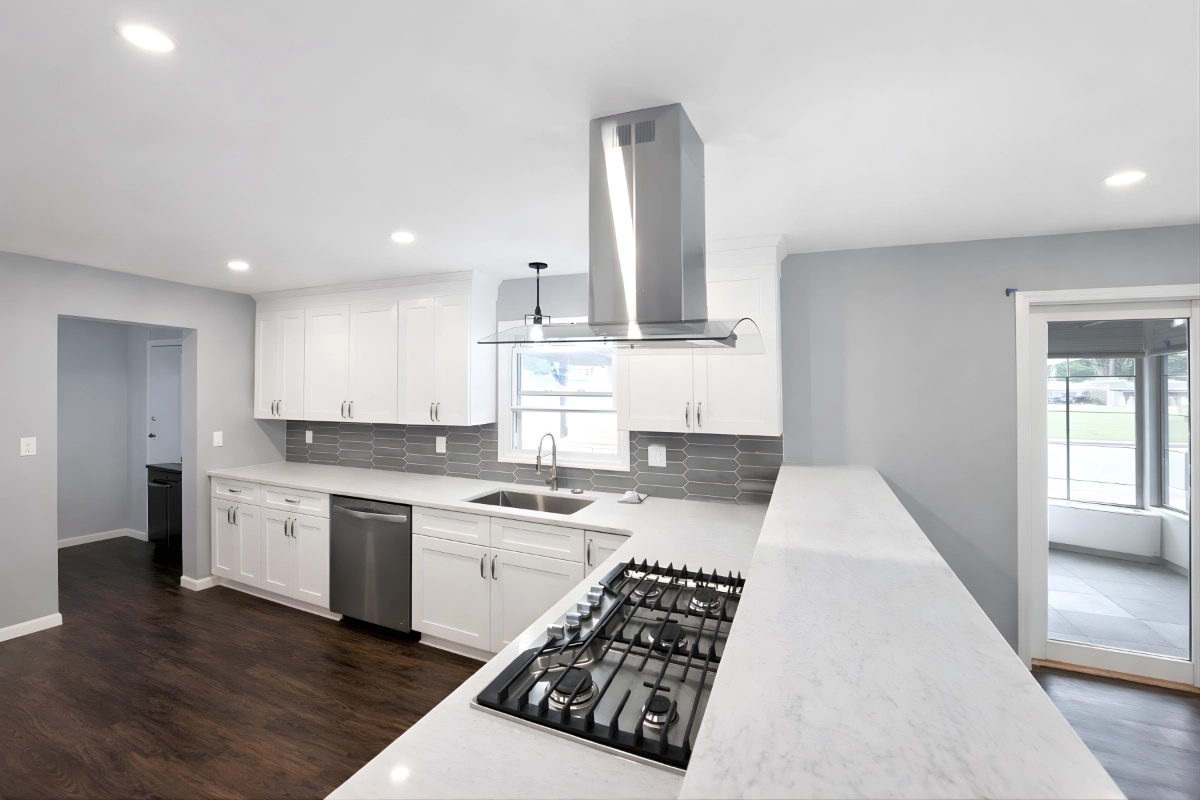 Completed modern kitchen remodeling project with white cabinets, island cooktop, and updated lighting in Berkeley Township, NJ.