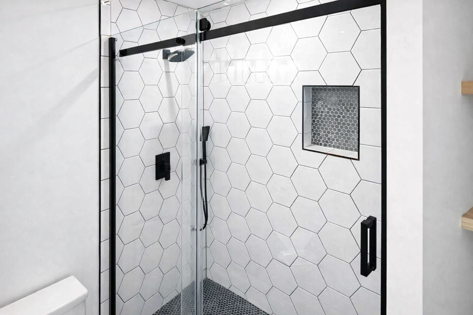 Custom walk-in shower as part of a bathroom remodeler project in Neptune City, NJ, featuring white hexagon wall tile, black hardware, and frameless glass doors.
